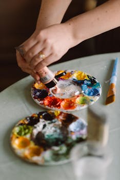 Colorful paint palette with hands preparing paint in a sunlit studio.