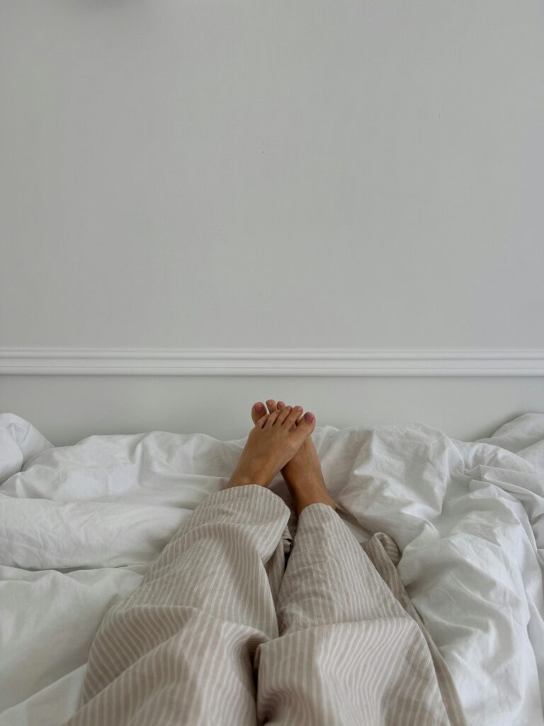 A pair of feet resting on a bed with white bedding, suggesting a calm and relaxed atmosphere.