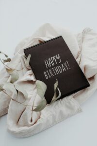 A birthday notebook with the words 'Happy Birthday!' on a light fabric background, adorned with a green leaf.